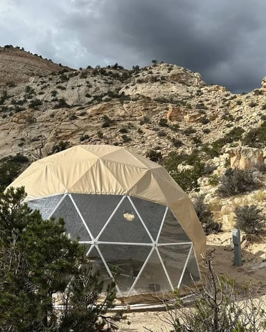Geodesic dome tent with tan rain fly in rocky desert canyon under stormy sky