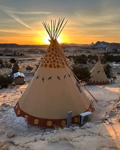 Decorated teepee with red and yellow polka dots in desert landscape at sunset, mountains in background
