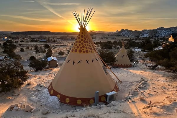 Decorated teepees in desert landscape at sunset with mountains and scattered buildings in background