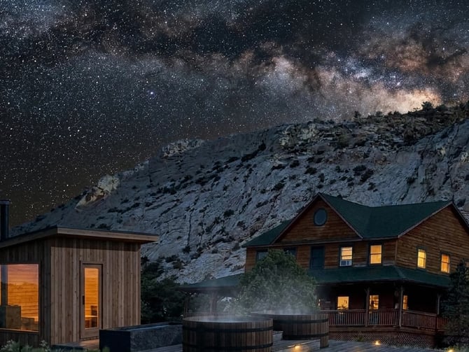Modern wooden cabin and sauna with hot tub under starry night sky and snowy mountain backdrop