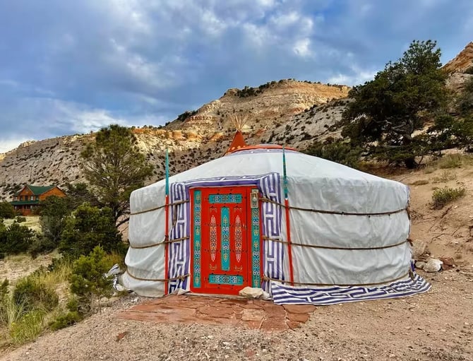 Decorative yurt with white canvas and ornate red door in arid desert landscape with rocky hills